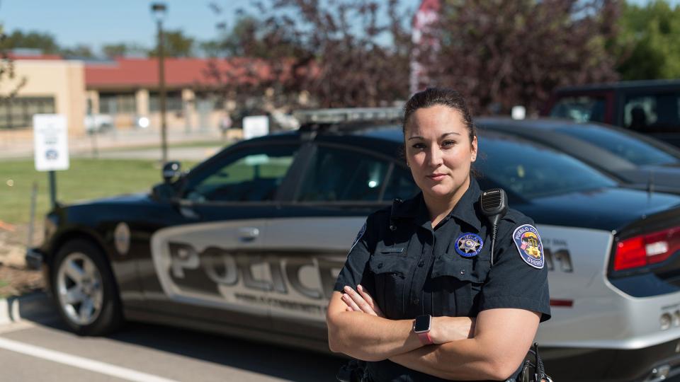 Female Law Enforcement Academy graduate standing in uniform in front of police car