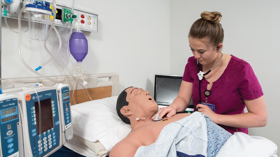 Nursing student using stethoscope on training mannequin