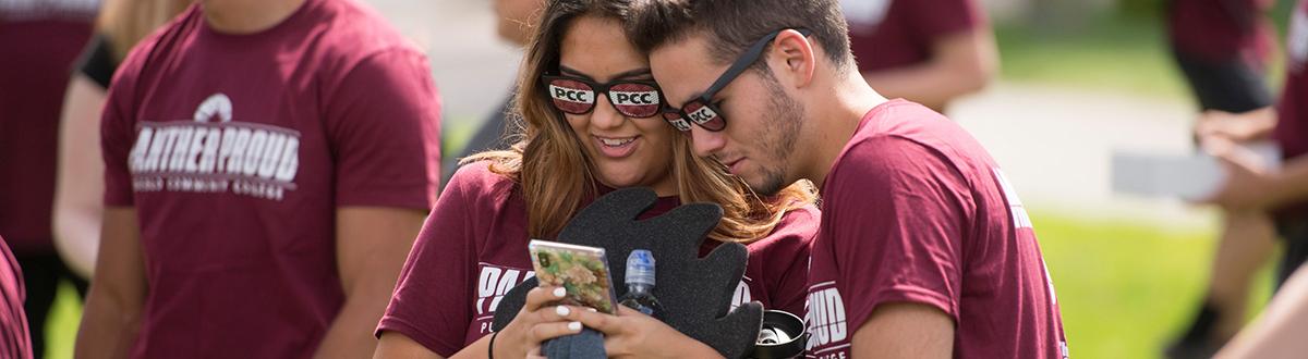 students looking at phone with PCC sunglasses on