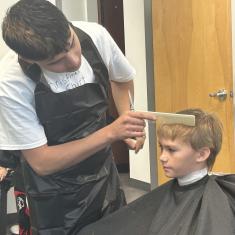 Cosmetology student cutting young boy's hair